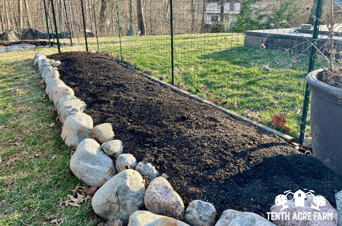 A new garden bed with a rock border has dark soil.